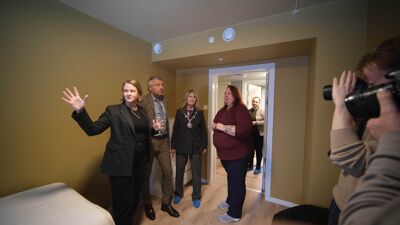 Fire mennsker står i et rom, de blir tatt bilde av av fortografer i bildekanten.