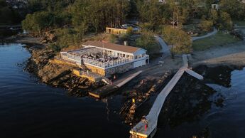 Illustrasjonsfoto som viser hvordan Hukodden strandrestaurant blir etter rehabiliteringsarbeidene. Bygget får blant annet et nytt inngangsparti med glasspartier mot terrassen, pergola over deler av terrassen, en ny glasskorridor som leder ut i hagestuen og nye store glassfoldevegger som kan åpnes opp mot terrassen.