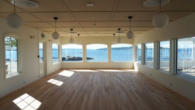 Viser spisesalen inne på Hukodden strandrestaurant, med store vinduer ut mot havet.