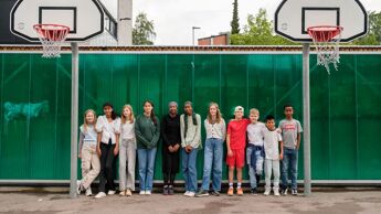 En gruppe skolebarn som står på en basketballbane i en skolegård mellom to basketballkurver.