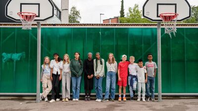 En gruppe skolebarn som står på en basketballbane i en skolegård mellom to basketballkurver.