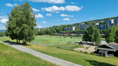 Bildet viser Rustad kunstgressbane litt på avstand, der flere er ute og spiller fotball.