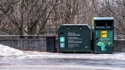 To grønne containere foran en mur og trær