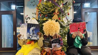 Tre mennesker sitter utkledd foran et juleferie. De dekker ansiktet med en bok.