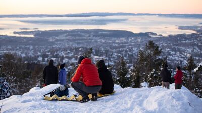 Folk nyter utsikten over et snødekket Oslo i solnedgangen fra Vettakollen