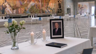 Bord med hvit duk og hvite roser, tente lys, bilde av kong Harald og kondolanseprotoll i Rådhushallen.