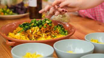 Vegetarisk middagsmat i en serveringstallerken. Skåler er satt fram. Hendr strekker seg mot maten.