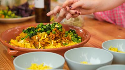 Vegetarisk middagsmat i en serveringstallerken. Skåler er satt fram. Hendr strekker seg mot maten.