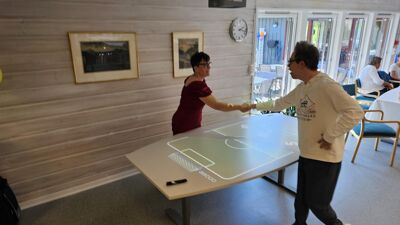 To personer hilser og smiler over et interaktivt bord med spilldesign.