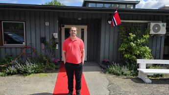 Mann står på rød løper foran inngangen til Poppelhuset med norsk flagg ved døren.