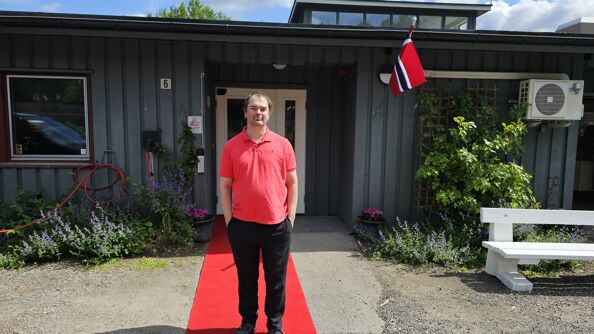 Mann står på rød løper foran inngangen til Poppelhuset med norsk flagg ved døren.