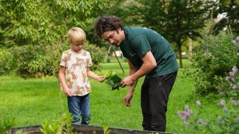 En gutt og en mann planter i en plantekasse.