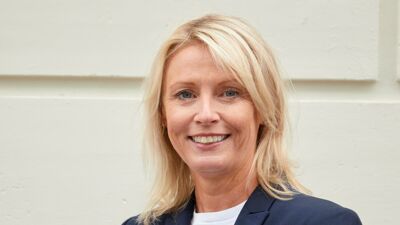 Bilde av bydelsdirektør Trine i mørkeblå jakke foran hvit vegg