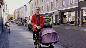 Mann i rød hettejakke triller barnevogn i Oslo sentrum.