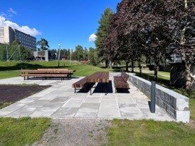 Utemøbler i over et område med asfalt ved siden av en blokk.