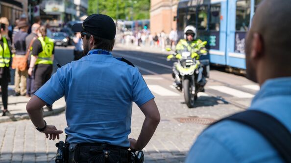 Bybilde - en politimann står med ryggen til i sentrum av bildet. Det er forskjellige folk rundt som ikke er like tydelige, og en trikk kjører på høyre side av bildet.