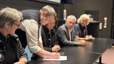 Aktører fra politikken og frivilligheten sitter bak et bord og signerer den nye avtalen