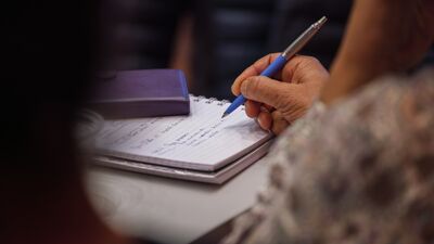 Sittende kvinne sett bakfra skriver i notatbok  med penn