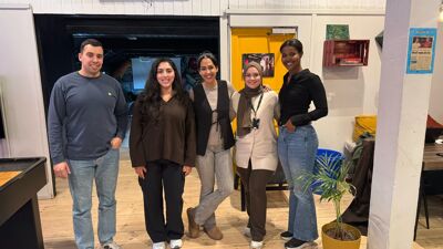 Fem voksne står ved siden av hverandre inne på ungdomsklubben Låven. De smiler og ser glade ut. ,