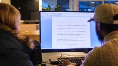 To personer sitter med ryggen til foran en dataskjerm. De skriver jobbsøknad