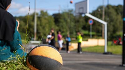 Jente sitter ved siden av basketball og ser på basketspillere på Tøyen.