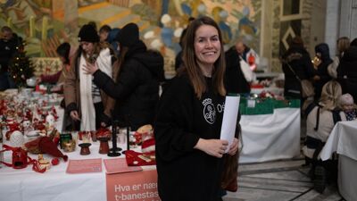 Kvinne med langt brunt hår foran et bord med julepynt. Det er folk i bakgrunnen.