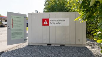 Grå container foran et buskas