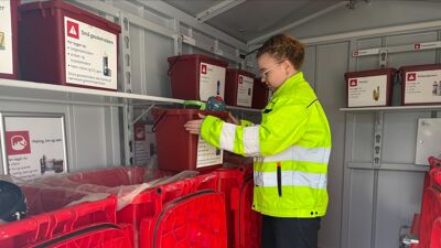 Dame i gul jakke ser oppi en rød plastboks