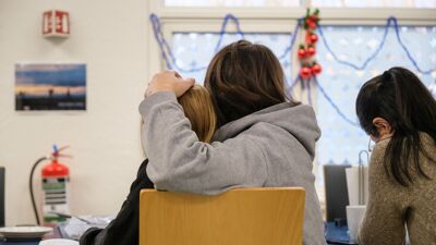 en mor og et barn sitter på en stol. moren holder rundt barnet. en annen person sitter til høyre for dem