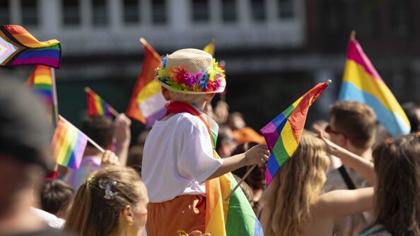 Pride-paraden 2023, et barn sitter på skuldrene til en voksen. Barnet holder et prideflagg.