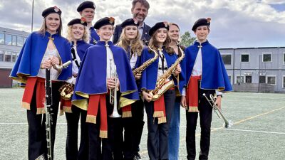 Skolekorpsmed 7 personer i uniform og en voksen mann og en kvinne