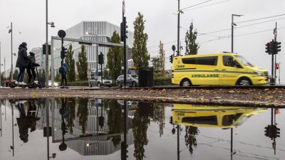 I front er et vannspeil, hvor en vei med en kjørende ambulanse speiles. I bakgrunnen er Deichmans hovedbibliotek.