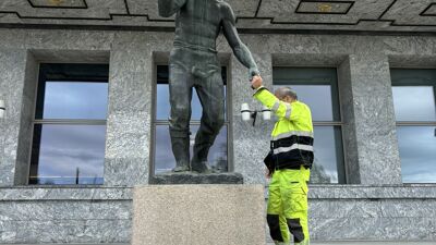Person i refleksbekledning inspiserer en bronseskulptur foran en steinbygning.