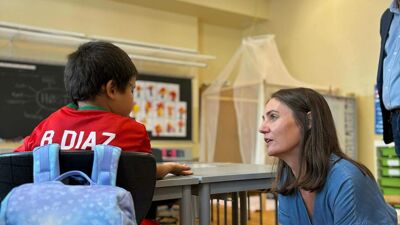 Skoleelev sitter med ryggen til med rød fotballskjorte. Utdanningsbyråden sitter på huk ved siden av og prater med eleven.