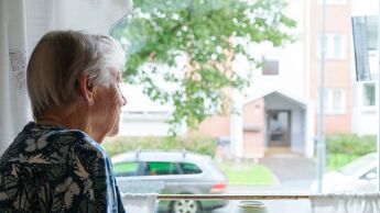 Bildet viser en eldre kvinne se ut av vinduet