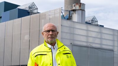 Mann i gul jakke foran fabrikkbygg