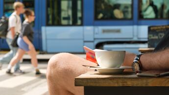 Mann drikker kaffe og leser bok mens trikken passerer.