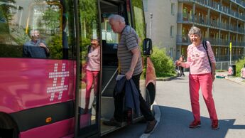 To eldre mennesker på vei inn i en rosa buss.