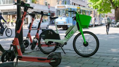 Elsparkesykler og elsykkel til leie parkert på fortauet. Trikk i bakgrunnen. Oslo sentrum.