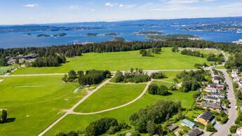 Oversiktsbilde av grønn slette. Oslofjorden i bakgrunnen.