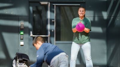Gutt kaster rosa ball til sosiallærer i skolegård. Hun tar i mot ballen med et bredt smil.