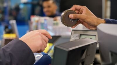 En hånd strekker seg fram over en disk i en butikk, for å ta i mot en snusboks som en annen person er i ferd med å gi fra seg.