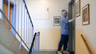 Kvinne i blå arbeidsuniform står utenfor en dør i en trappeoppgang og ringer på.