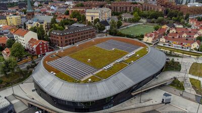 Jordal amfi sett overnfra. Det er gress på taket og i bakgrunnen er boligbyggene på Kampen.