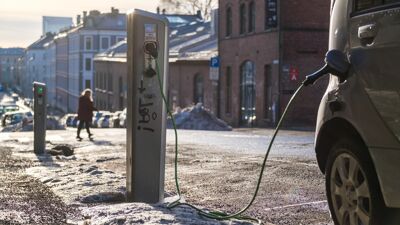 Gate i vinterlys, med ladestasjon, og ladekabel som går inn i en bil.