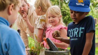 Barnehagebarn samlet rundt et bord med krydderplanter og en morter.
