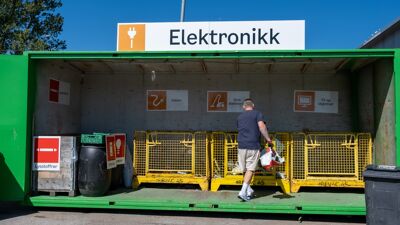Grønn container med åpne dører, gule metallbur inni.