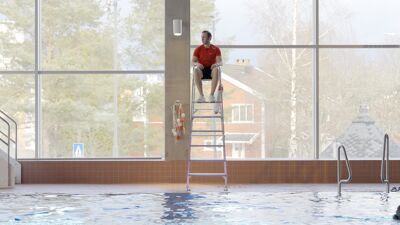 En badevakt sitter på stolen og ser på bassenget.