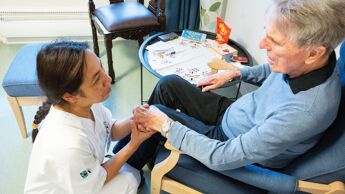 Eldre mann på sykehjem holder pleier i hånden