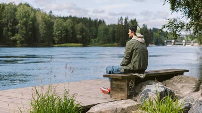 Mann sitter på en benk og ser utover et vann.